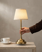 Pleated Brass cordless lamp, brass stem, pleated shade, USB-C dimmer, 40 cm — in use, hand on the brass stem | Dalfa CH/FR