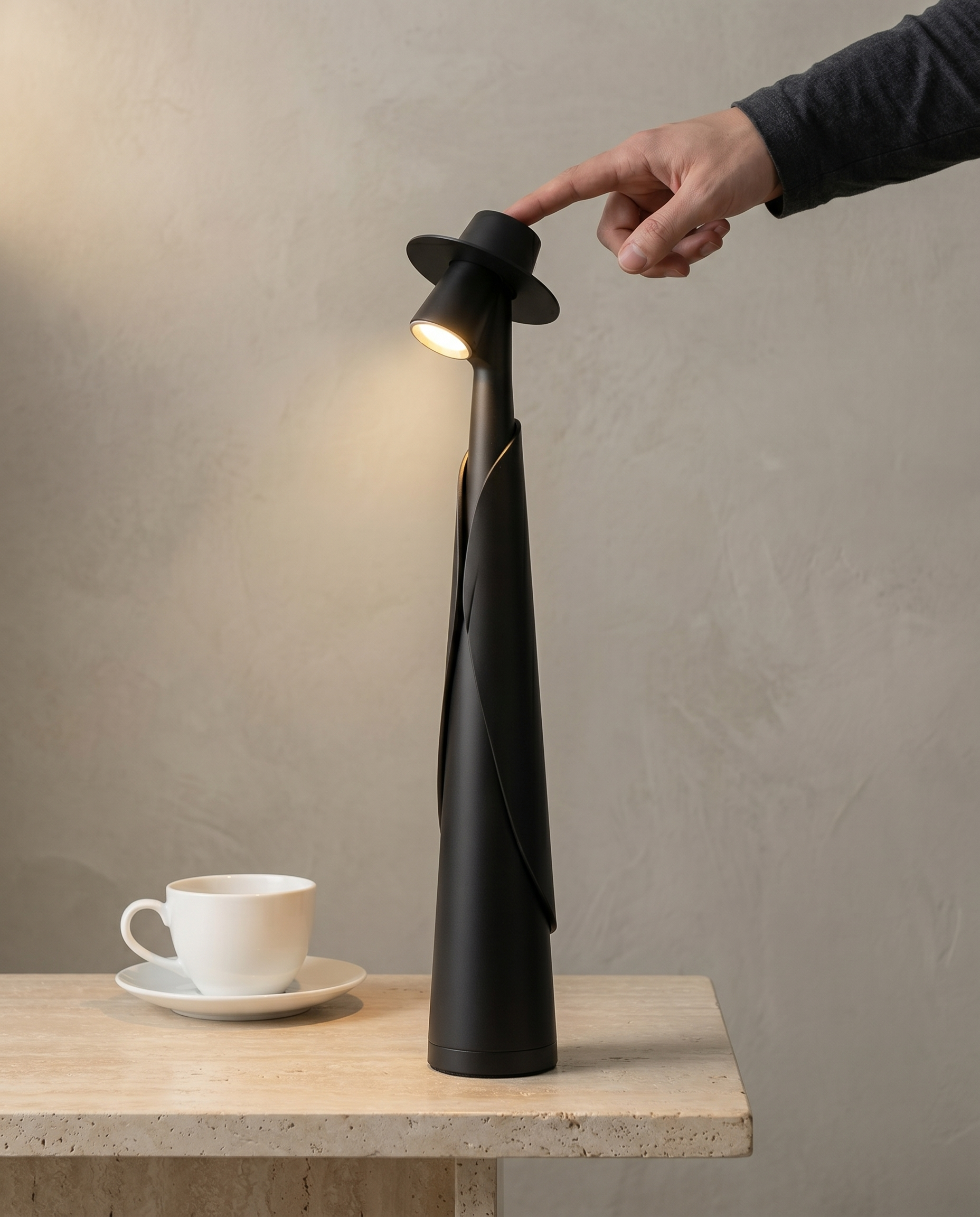 Hand touching the hat switch of a matte black figure lamp, warm spotlight on, on travertine — Dalfa CH/FR