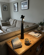 Matte black figure lamp lit on a desk with a book and mug in an ordinary living room — Dalfa CH/FR