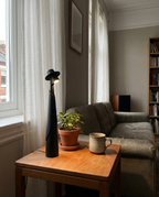 Matte black figure lamp lit on a side table by a window with a plant, real living room — Dalfa CH/FR