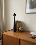 Matte black figure lamp off on a wooden sideboard with books and a vase, real home — Dalfa CH/FR