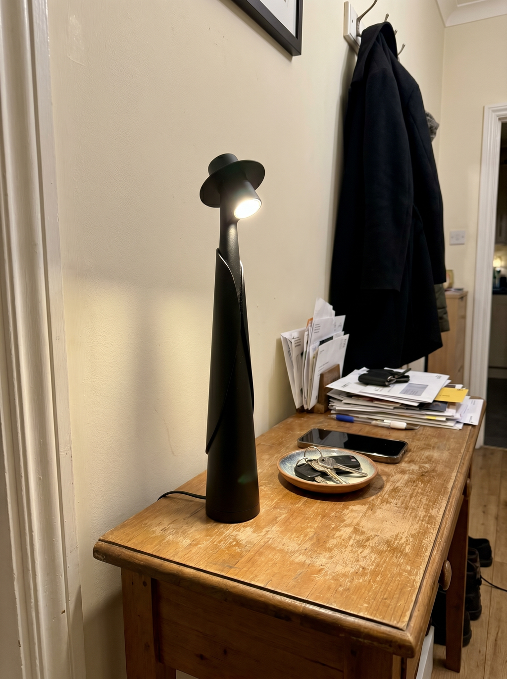 Matte black figure lamp lit on a hallway console with keys and a coat, real home — Dalfa CH/FR