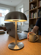 Brushed steel dome lamp lit on a home-office desk beside a laptop and mug — Dalfa CH/FR