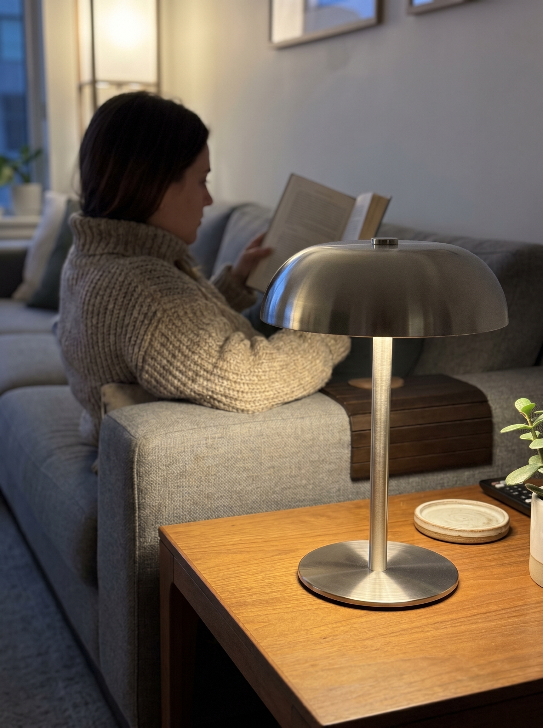 Brushed steel dome lamp lit on a coffee table while a person reads on the sofa — Dalfa CH/FR